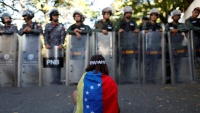 Jedna djevojka s venecuelanskom zastavom naspram interventnih policijskih snaga u Karakasu