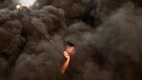 Palestinski prosvjednik u trenutku bacanja kamena obavijen dimom