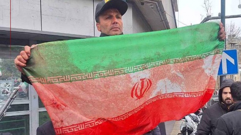 Iranski policajac drži krvlju umrljanu zastavu žene ubijene u američko-izraelskom napadu na Dan Kudsa u Teheranu, 13. marta 2026.